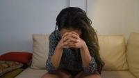 Woman sits on a sofa with her head in her hands